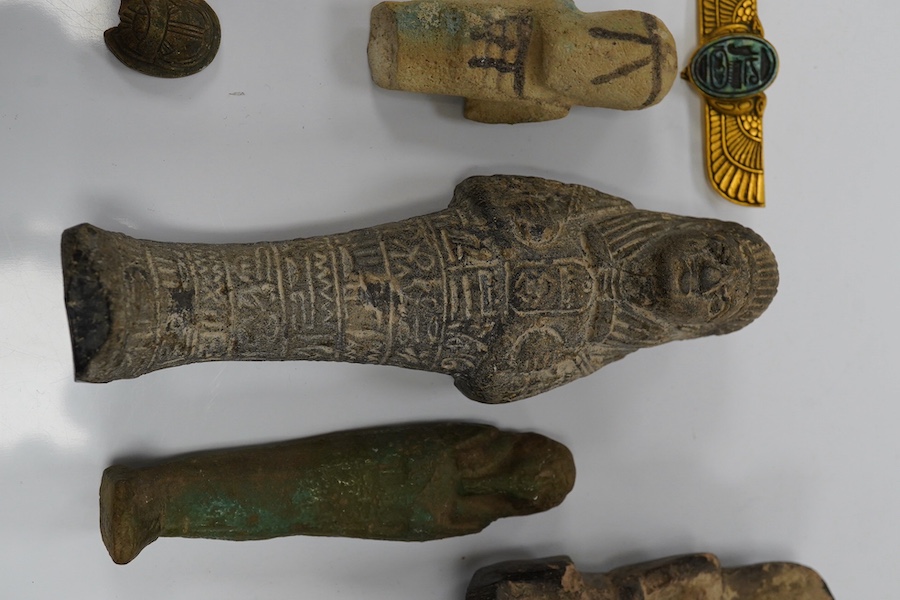 Three ancient Egyptian carved stone ushabti, tallest 15cm, with carved hieroglyphs to the body, together with a seated figure, possibly of Isis, a scarab and a yellow metal brooch with inset stone carved with hieroglyphs